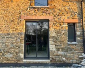 Façade en pierre rénovée à Saint-Aubin-du-Cormier avec création d'une ouverture pour baie vitrée et linteaux en bois par BF Maçonnerie